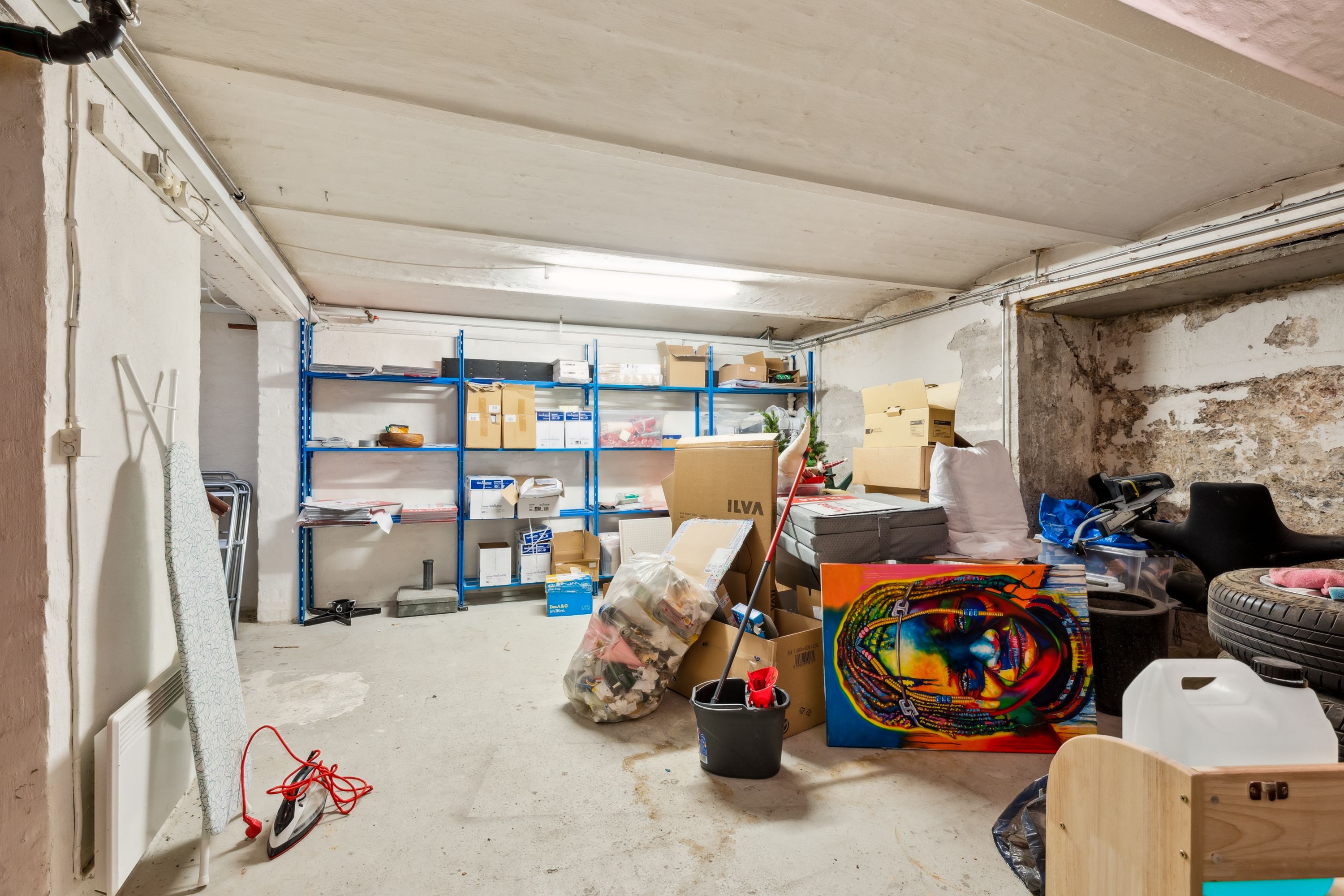 Et garagerum med tøjstativet, malingsbøtter, malerskeer og forskellige kasser og pakker, herunder en stor maleri-lærred med