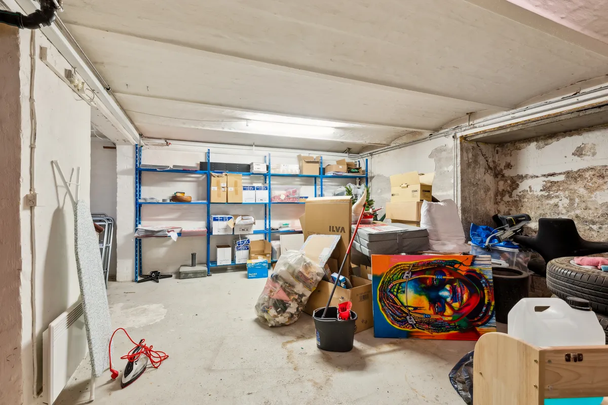 Et garagerum med tøjstativet, malingsbøtter, malerskeer og forskellige kasser og pakker, herunder en stor maleri-lærred med