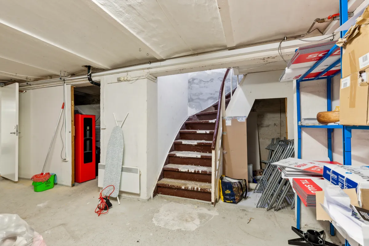 Lejemålets kælderrum med trapper, stiger og opvask, samt flere bokse og rengøringsprodukter på hylden