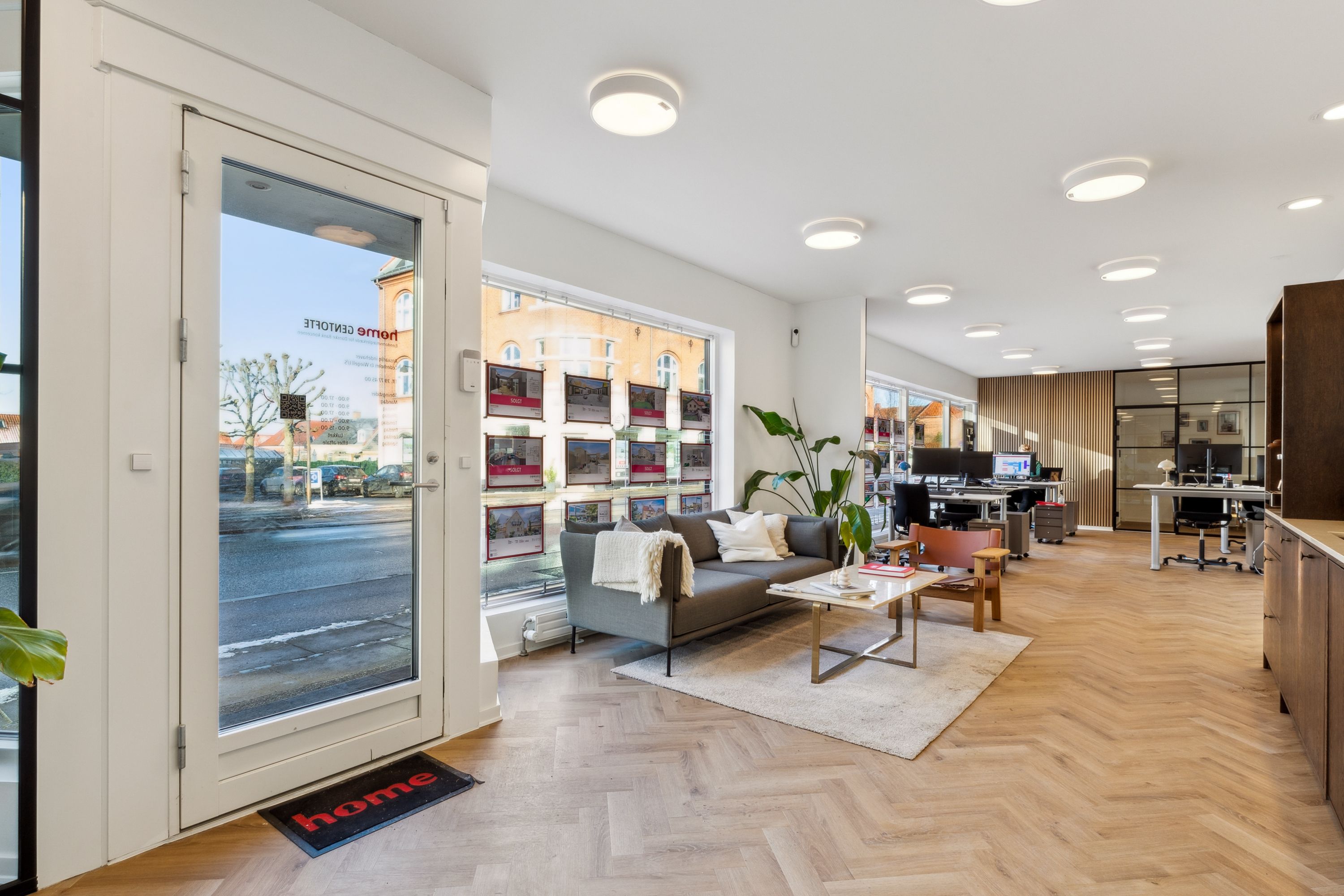 Indgangsdør til lejlighed med sofa og skrivebord, fuld af lyse og moderne møbler, skrivebord og lysekroner på loftet