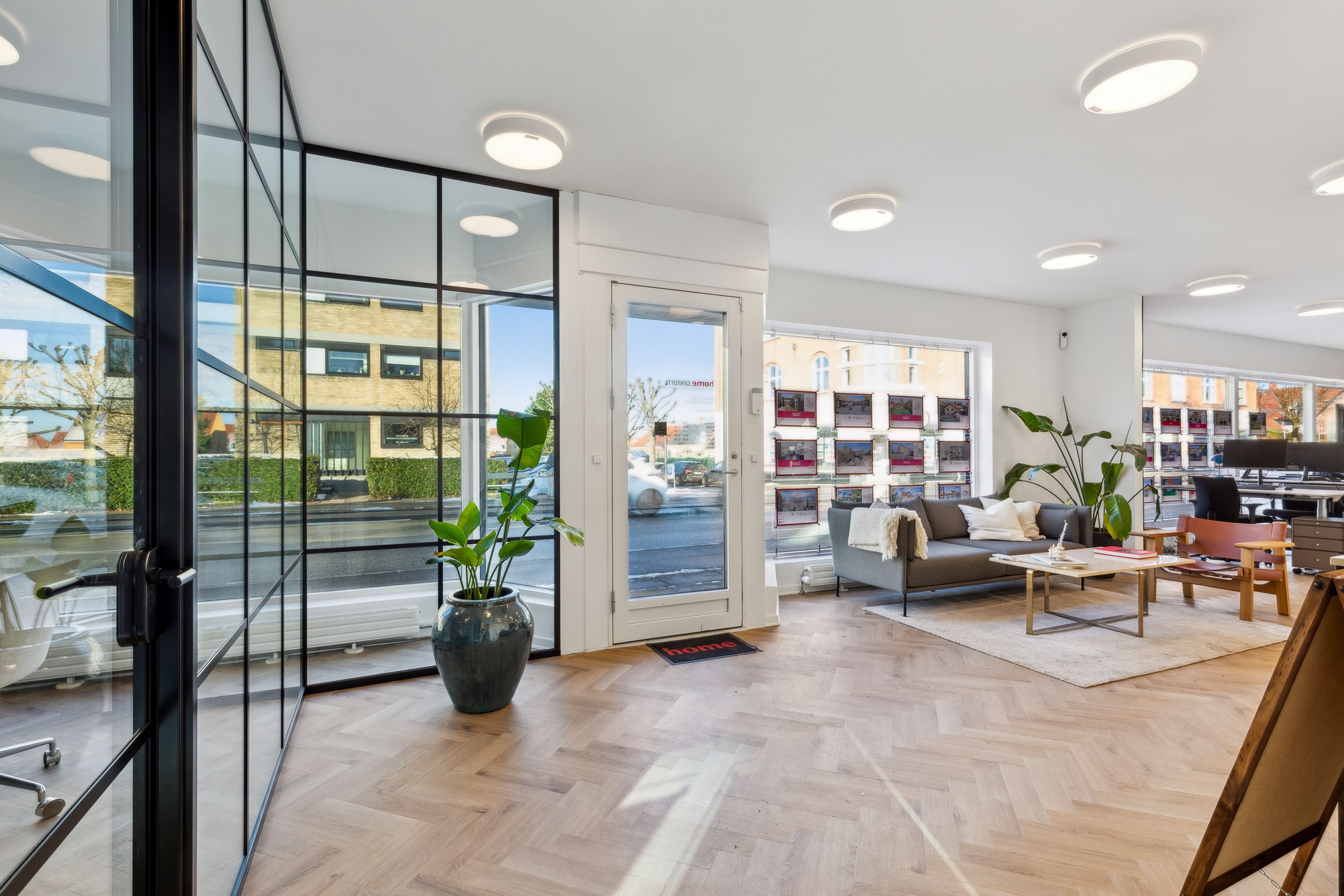 Moderne lobby med høje glasvinduer, indret med lyse loftslamper og møbler, herunder sofa, træbord, lænestol og stol, samt