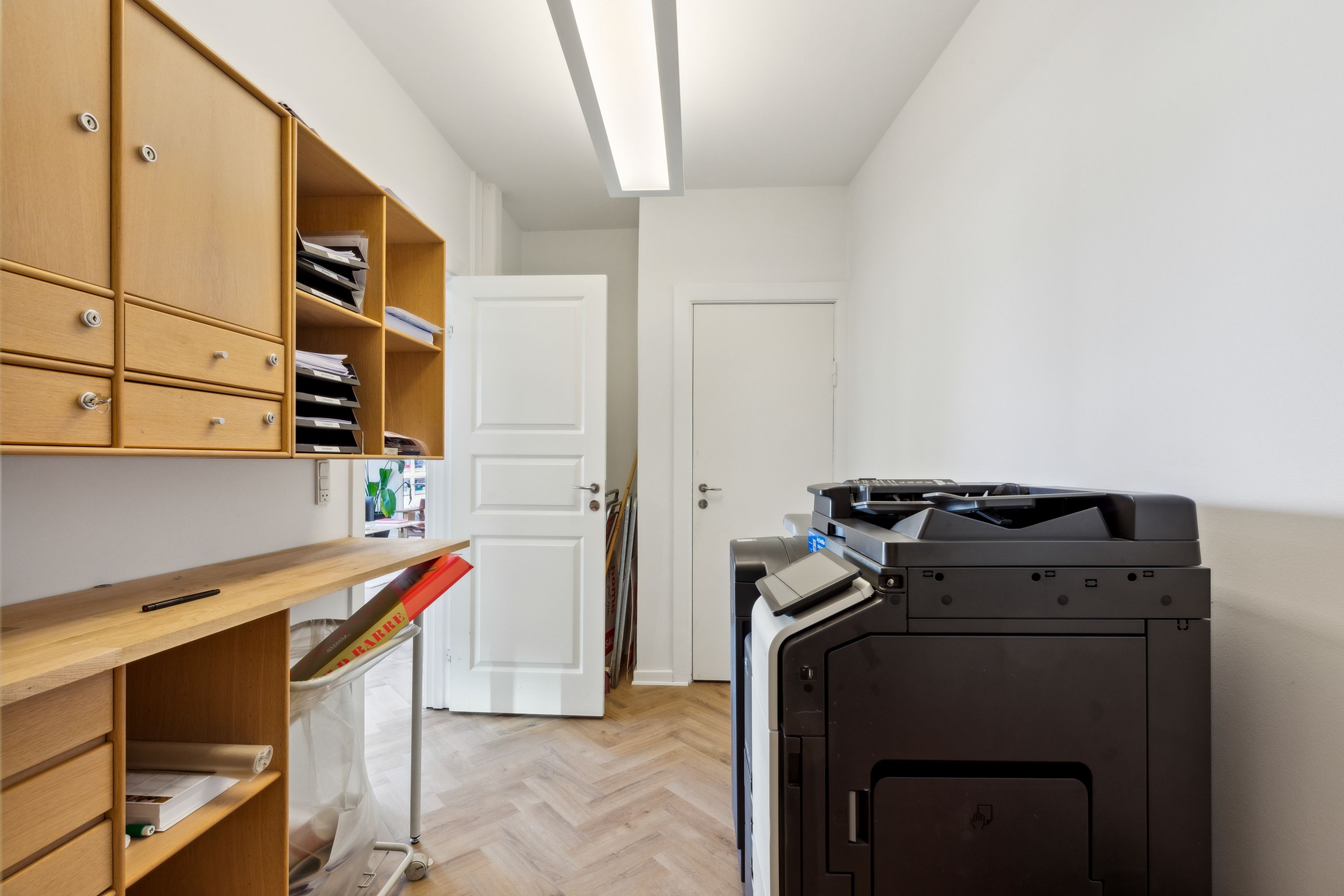 Foto af en tom kontorrum med en stor sort printer, hvidt loft, gulv og vægge samt et skur og to døre