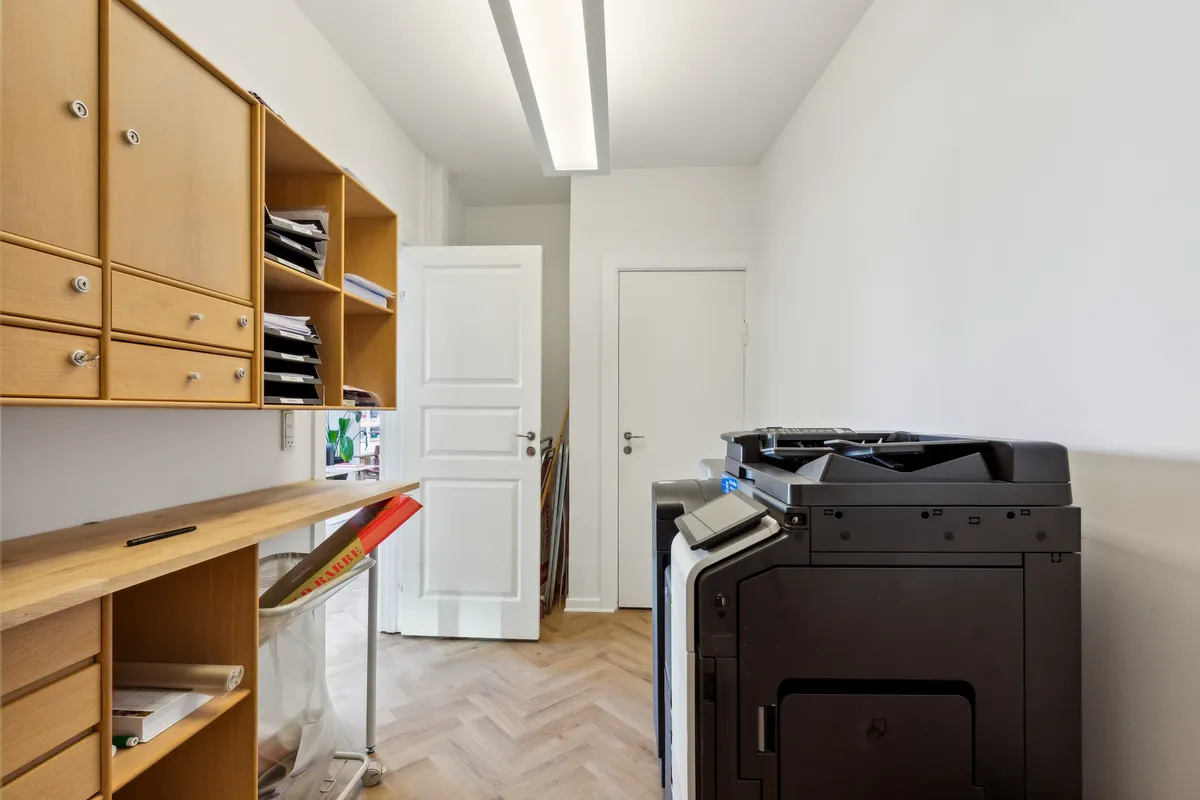 Foto af en tom kontorrum med en stor sort printer, hvidt loft, gulv og vægge samt et skur og to døre