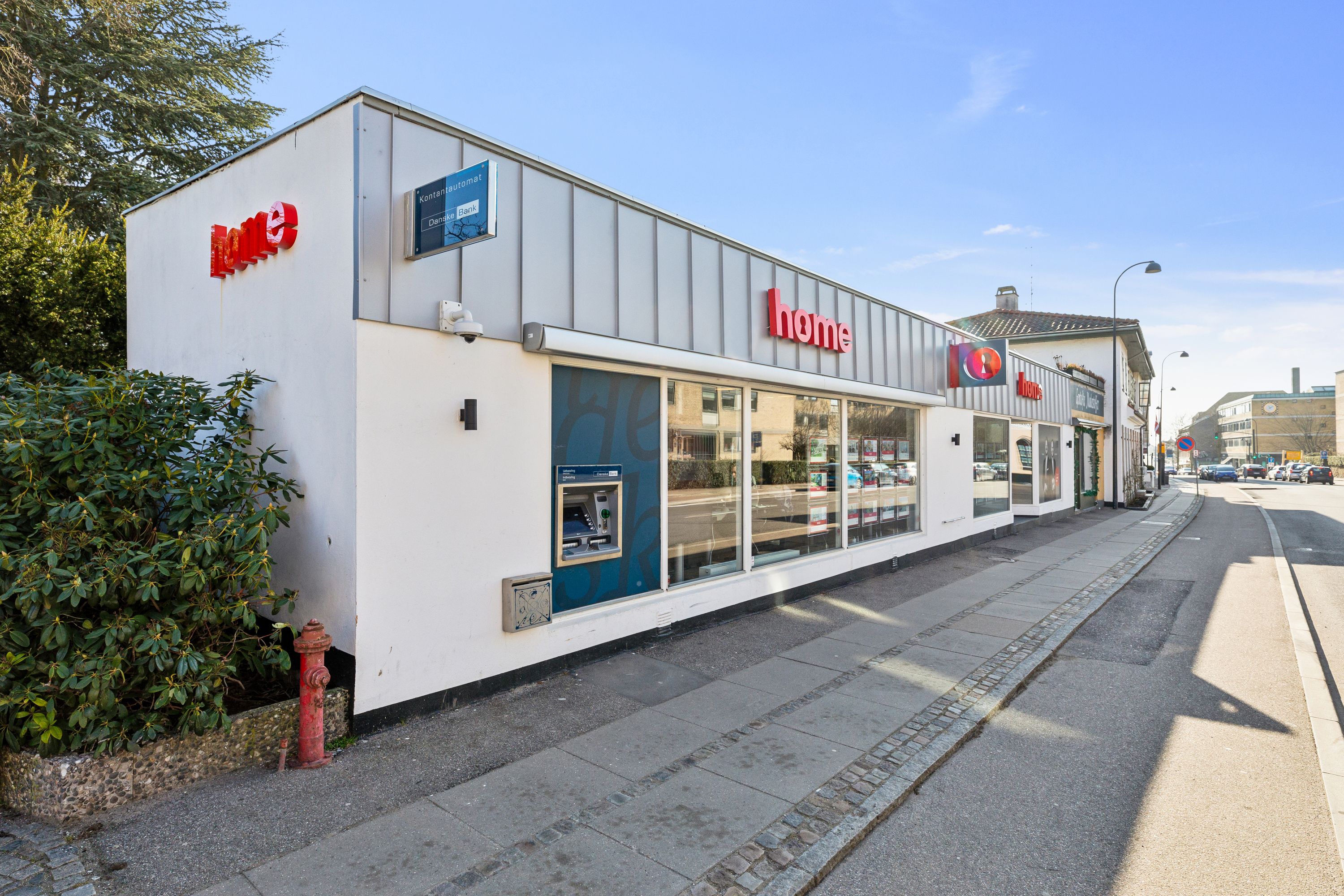 Hjørnebygning med lejetskiltet Home og ATM-automat samt en brandhåndtag og et rødt søjlelys på gaden