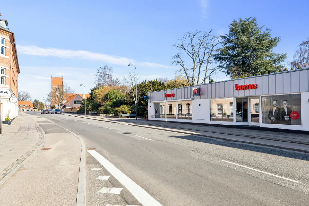 To ejendomme med store vinduer og reklameskilte med teksten Home og to mænd. Gaden er tom med enkelte biler parkeret i