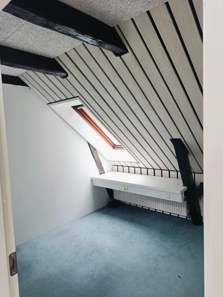 Et lille rum med et loft med lyse og mørke bjælker og en terrasse med gult gulv