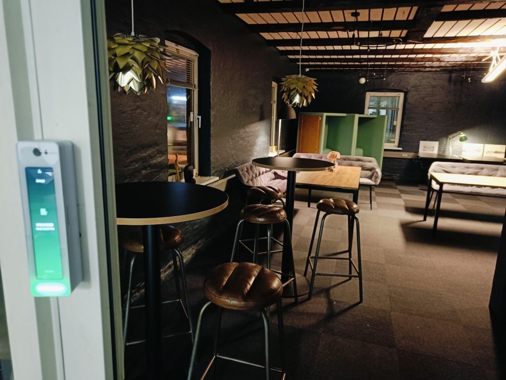 Interiør med møbler, herunder stole, borde, sofaer og vægmontreret lys. Kølige farver og moderne designelementer.