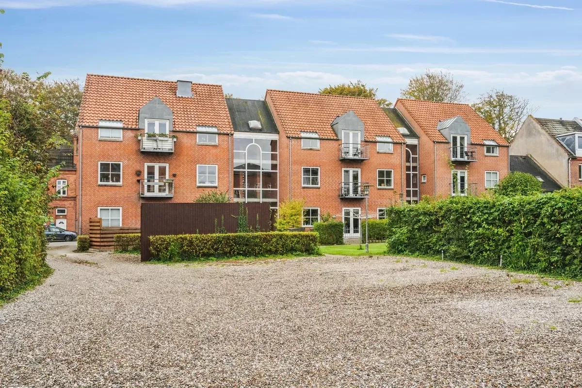 En række ejerlejligheder med terrasser og buske udenfor i en koldinggade med et parkeringsområde