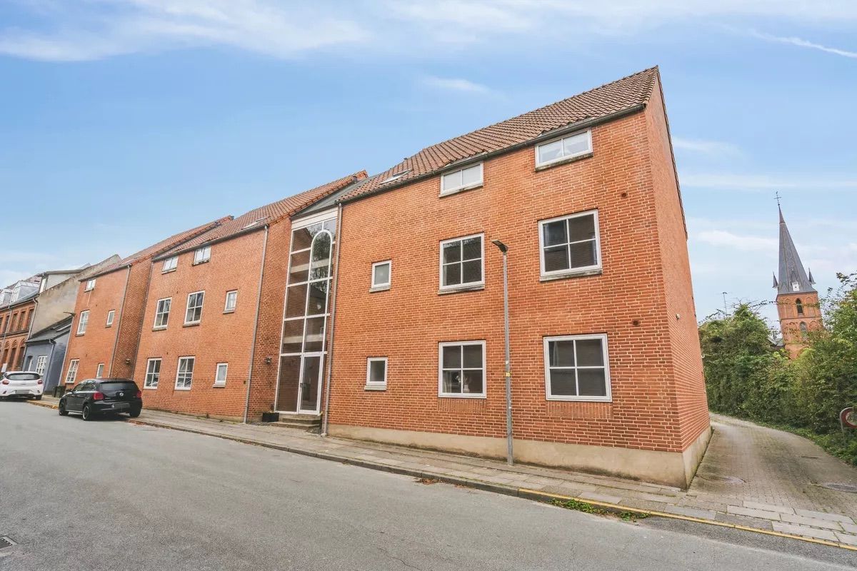 En stor rødmaursten bygning med flere lejligheder og flere parkerede biler langs gaden