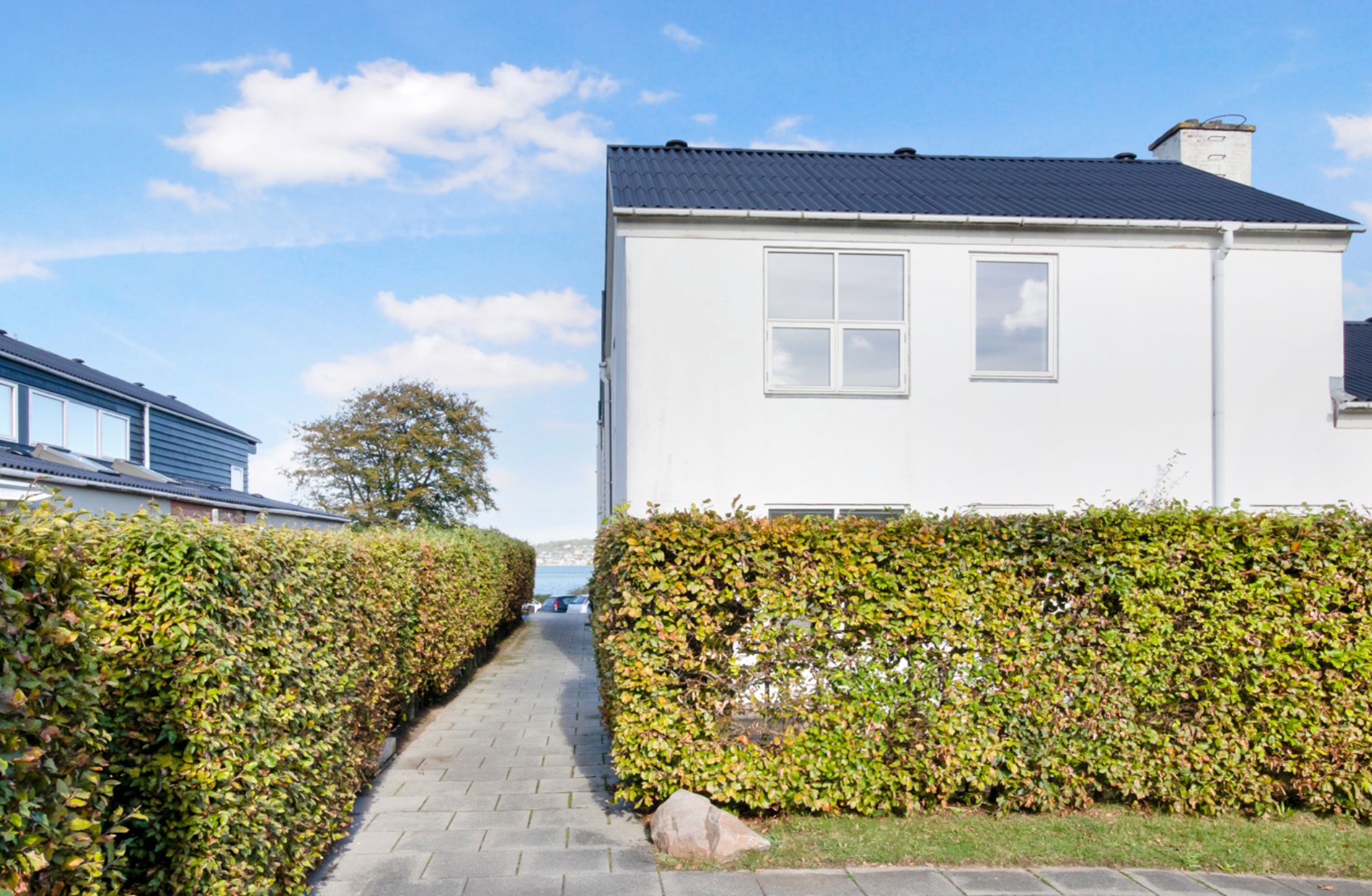 Ny rækkehus med terrasse og have på sydsiden af Kolding Fjord. Foran huse og hegn. Det er fint vejr med skyer på himlen.