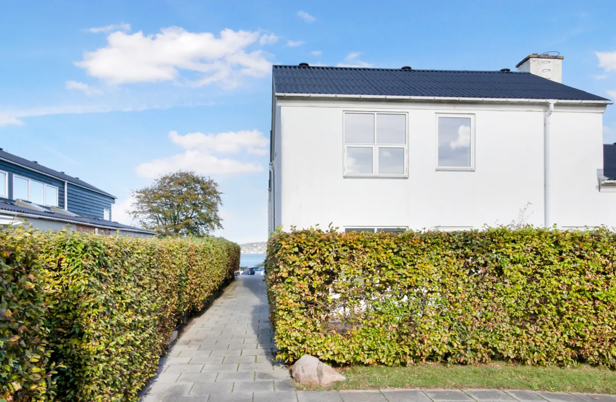 Ny rækkehus med terrasse og have på sydsiden af Kolding Fjord. Foran huse og hegn. Det er fint vejr med skyer på himlen.