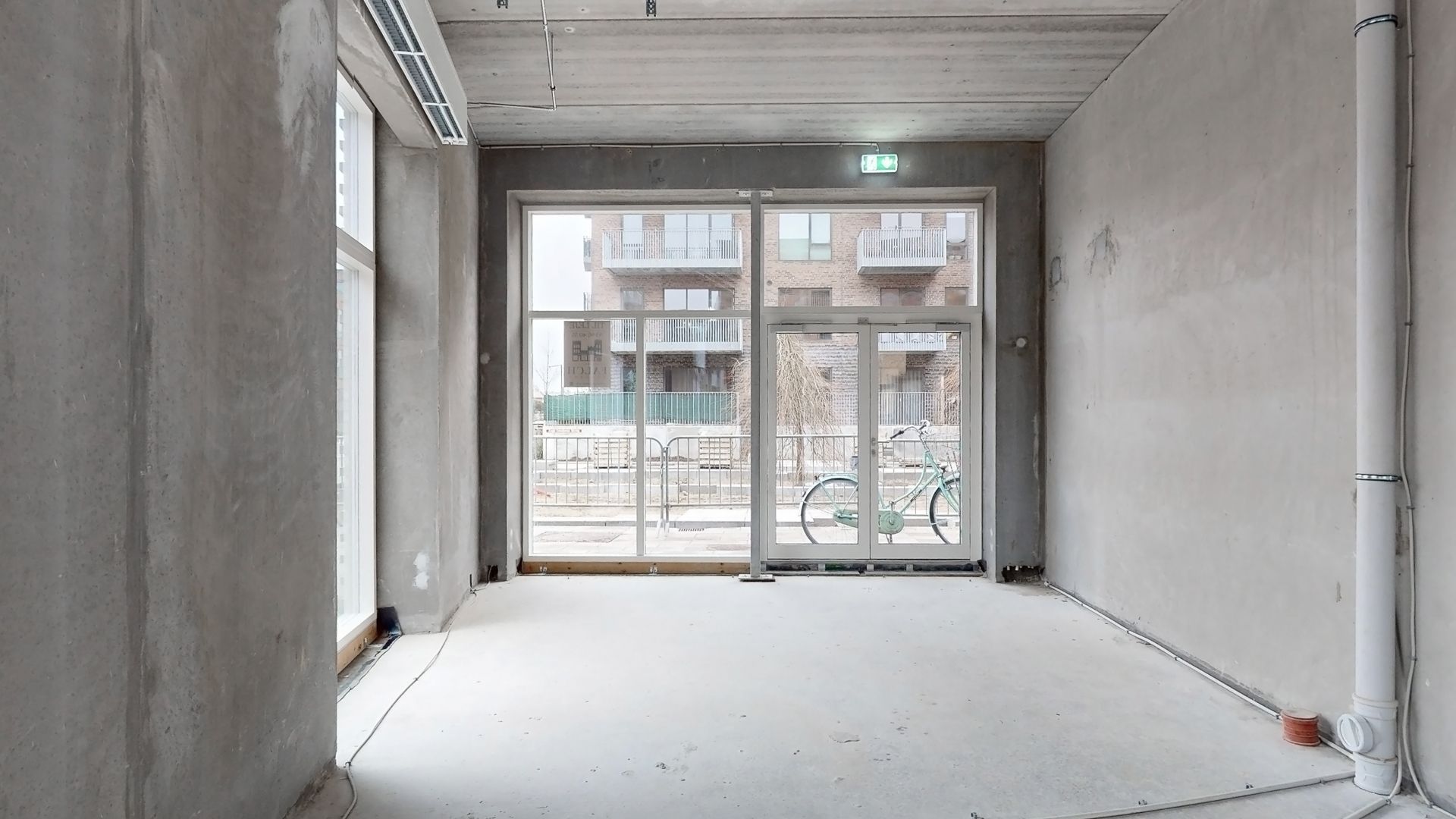 En stor glasdør og vinduer i en ny bygning med et hulloft og betonvægge