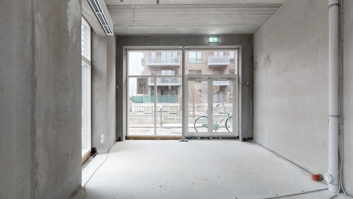 En stor glasdør og vinduer i en ny bygning med et hulloft og betonvægge