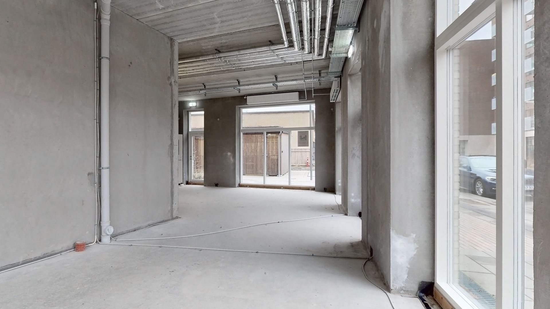 Ufuldendte kontorlokaler med hvide gulvbelægning og kontorvinduer, der vender ud mod en gågade med biler og huse