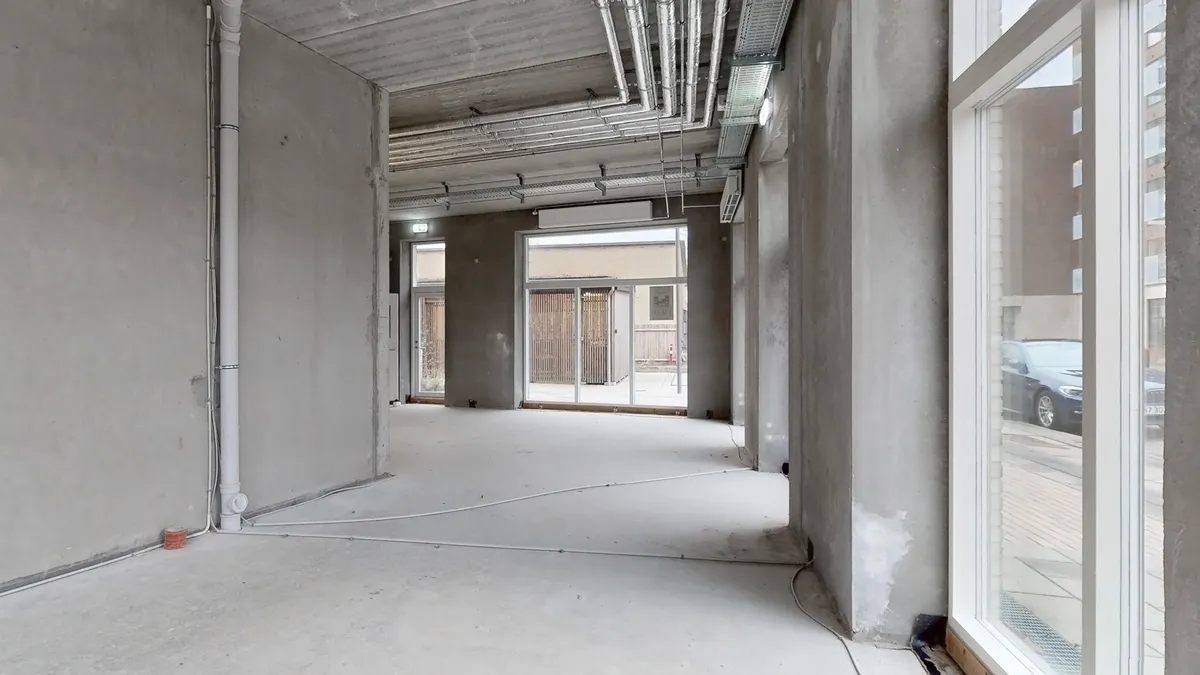 Ufuldendte kontorlokaler med hvide gulvbelægning og kontorvinduer, der vender ud mod en gågade med biler og huse