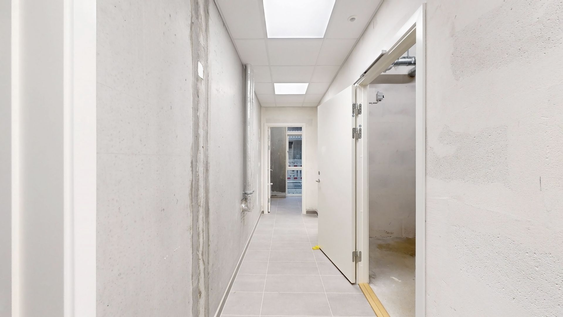Et langt og smalt, lysegråt og pænt hulrum med hvide vægge, gulv og loft samt åbne døre og en indgangsdør i hvidt og sølv