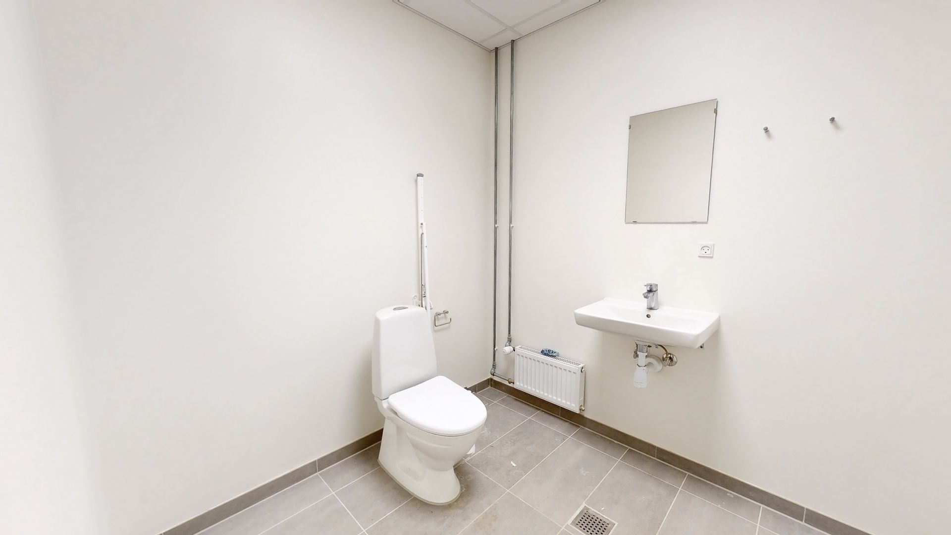 Ledig toiletrum med hvid toilet, spejl og hvidt vask. Det er lyse og rummeligt med gulvbelægning og hvid væg.