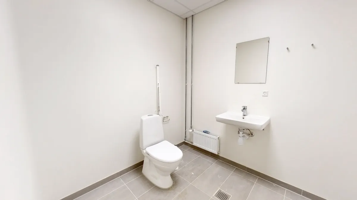 Ledig toiletrum med hvid toilet, spejl og hvidt vask. Det er lyse og rummeligt med gulvbelægning og hvid væg.