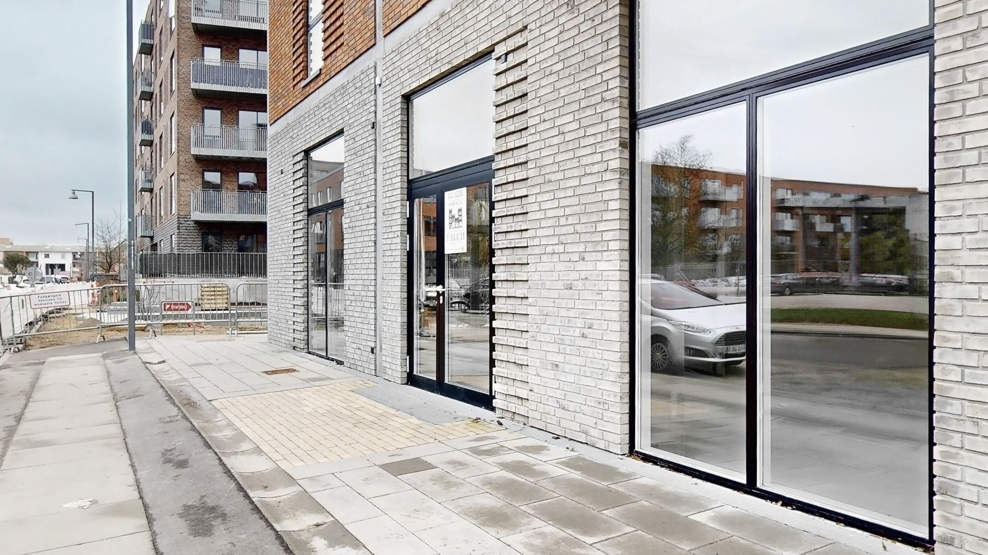 En stor bygning med glasvinduer og gule mursten og to biler parkeret på gaden med en forbudsskilt