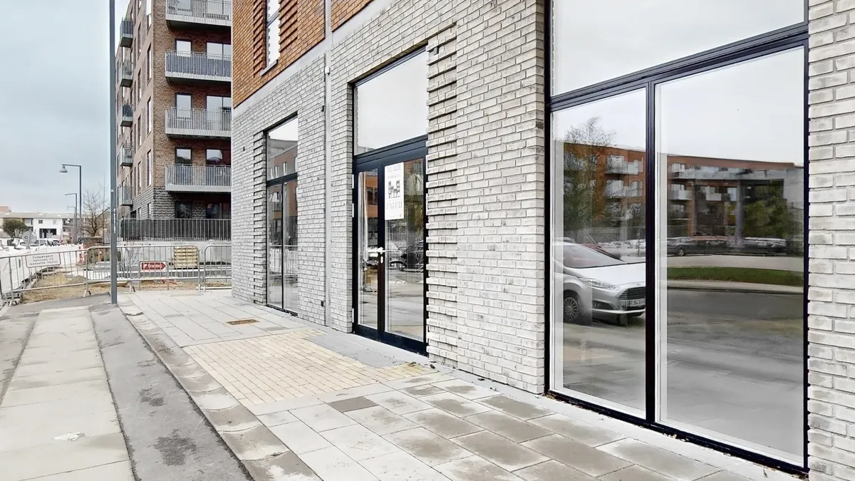 En stor bygning med glasvinduer og gule mursten og to biler parkeret på gaden med en forbudsskilt