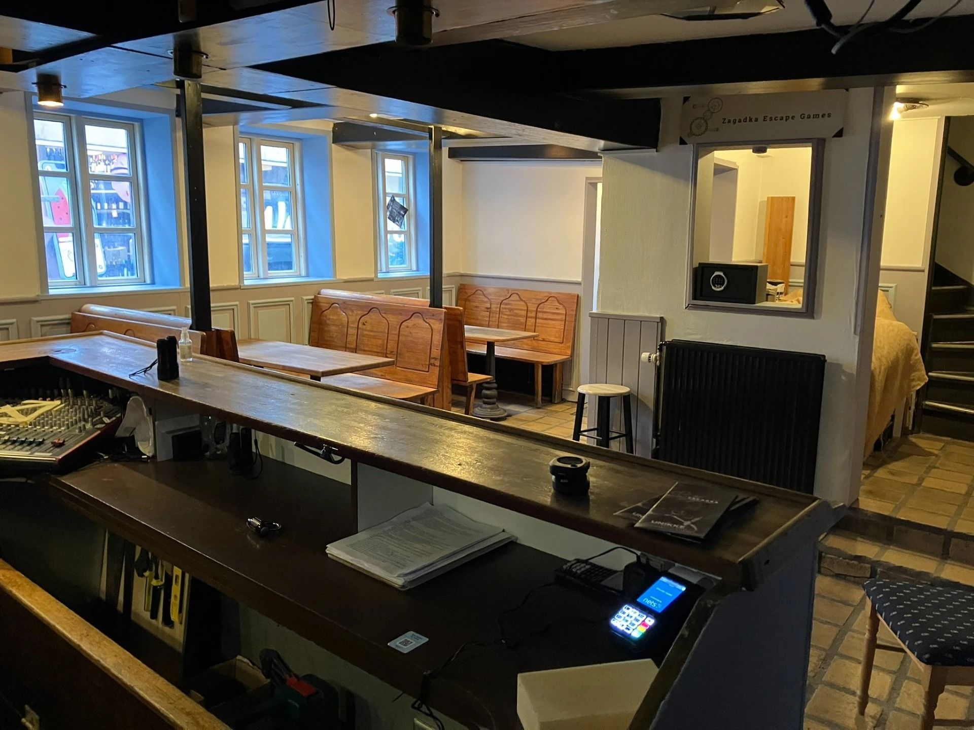 Inde i et hyggeligt lokale med træbænke og møbler, en høj bar og en kasse med en telefon samt en række elektroniske enheder