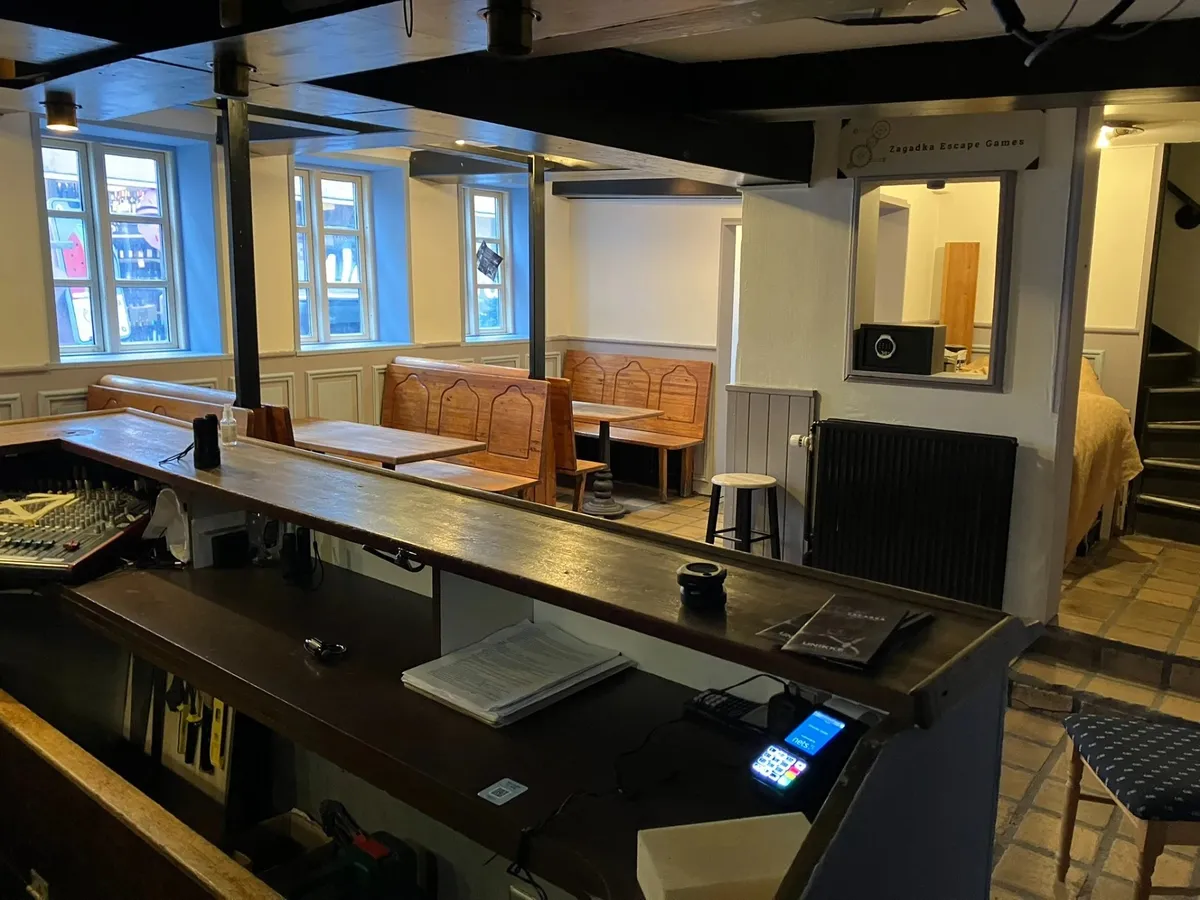 Inde i et hyggeligt lokale med træbænke og møbler, en høj bar og en kasse med en telefon samt en række elektroniske enheder