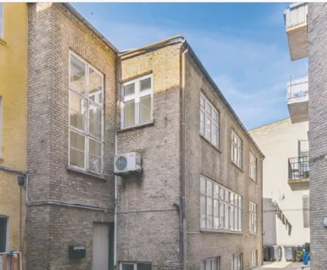 Kontorbyggeri med facade i brun tegl og glasruder og klimaanlæg i hjørnet mellem 2 bygninger på baggrund af blå himmel