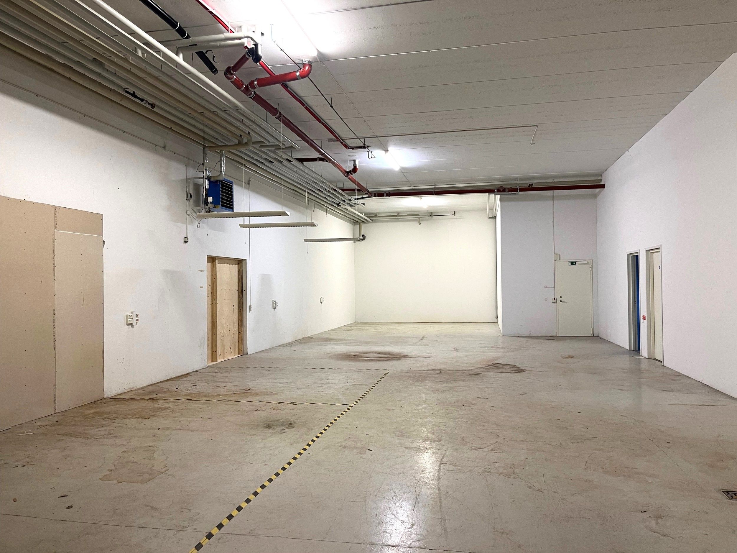 Stor industrilokale til leje med to porte og 4 meter til loftet, gulve med stribet sikkerhedsmærkning og flere luftkanaler