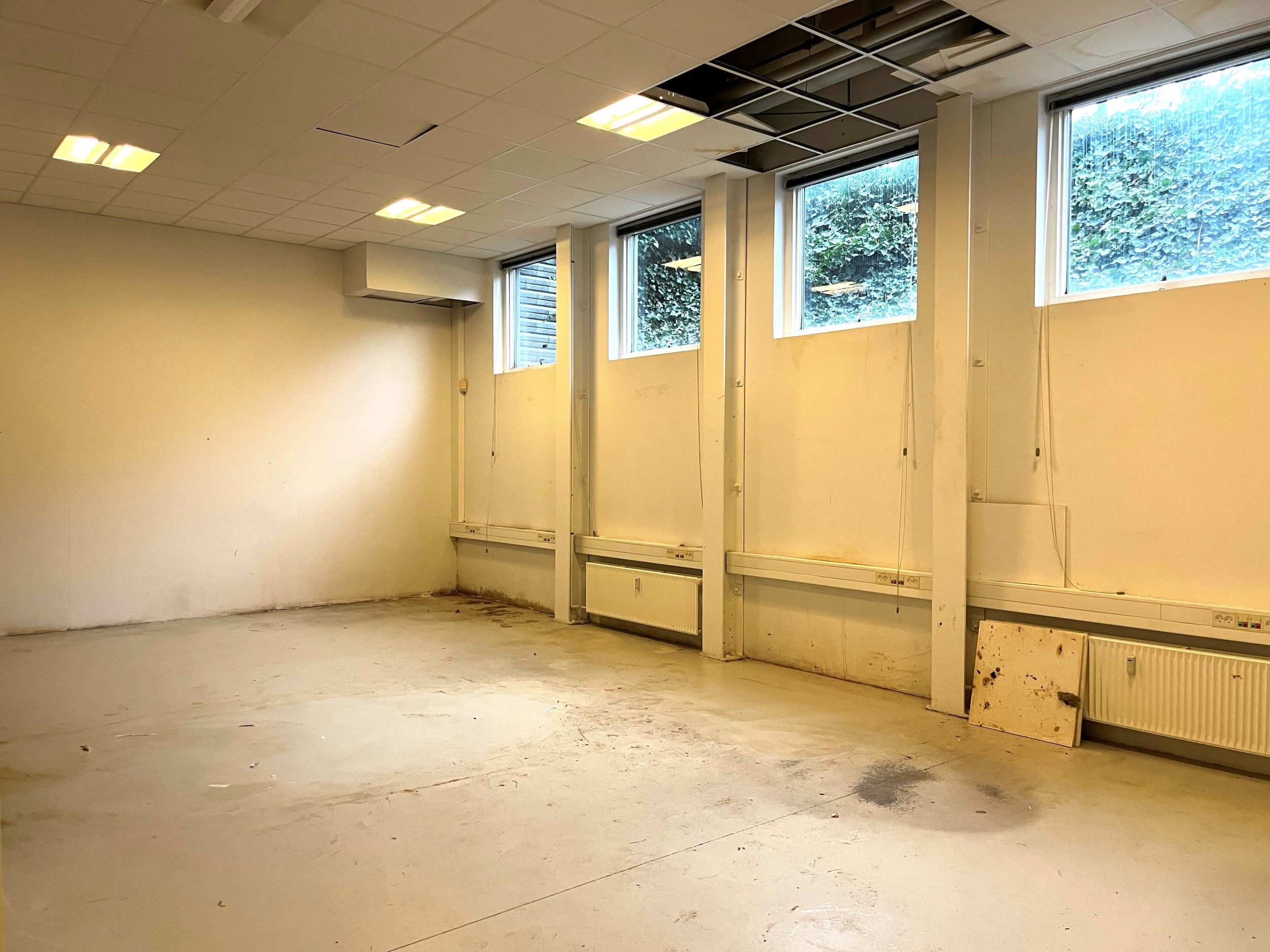 Tomt værelse med hvide vægge og loft, samme farve på gulvet og tre vinduer i den ene væg