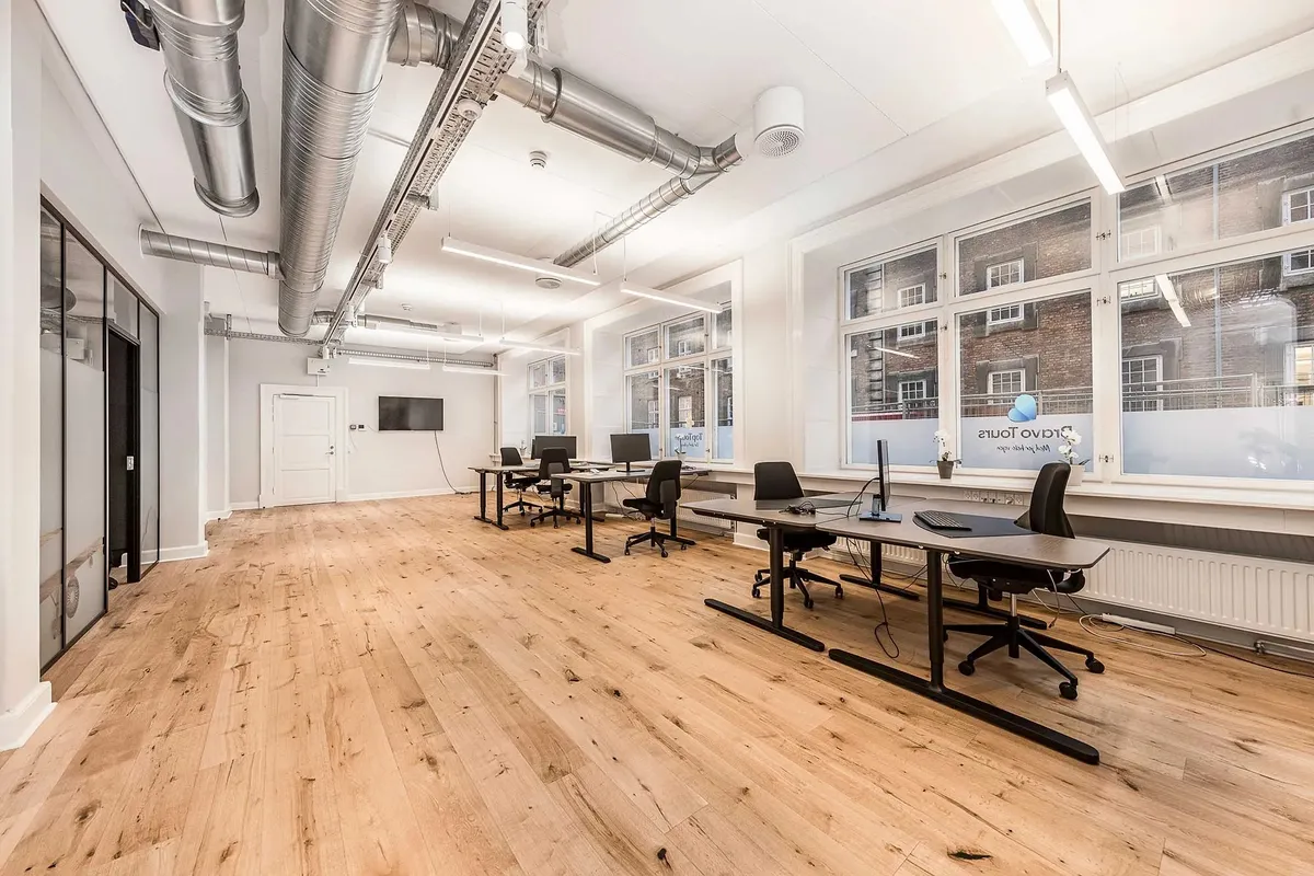 Kontor med lyse, høje vinduer, moderne møbler og hårde trægulve samt hvide vægge og store vinduer mod gaden