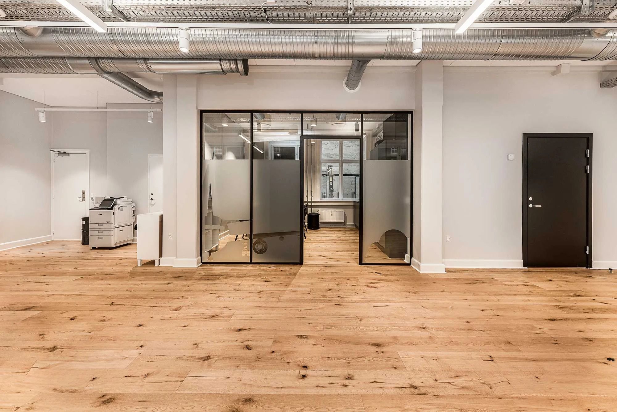 En luksuriøs kontorrum med højt til loftet, hvidt vægmaleri og lyse trægulve. Værelse med moderne glasdøre og