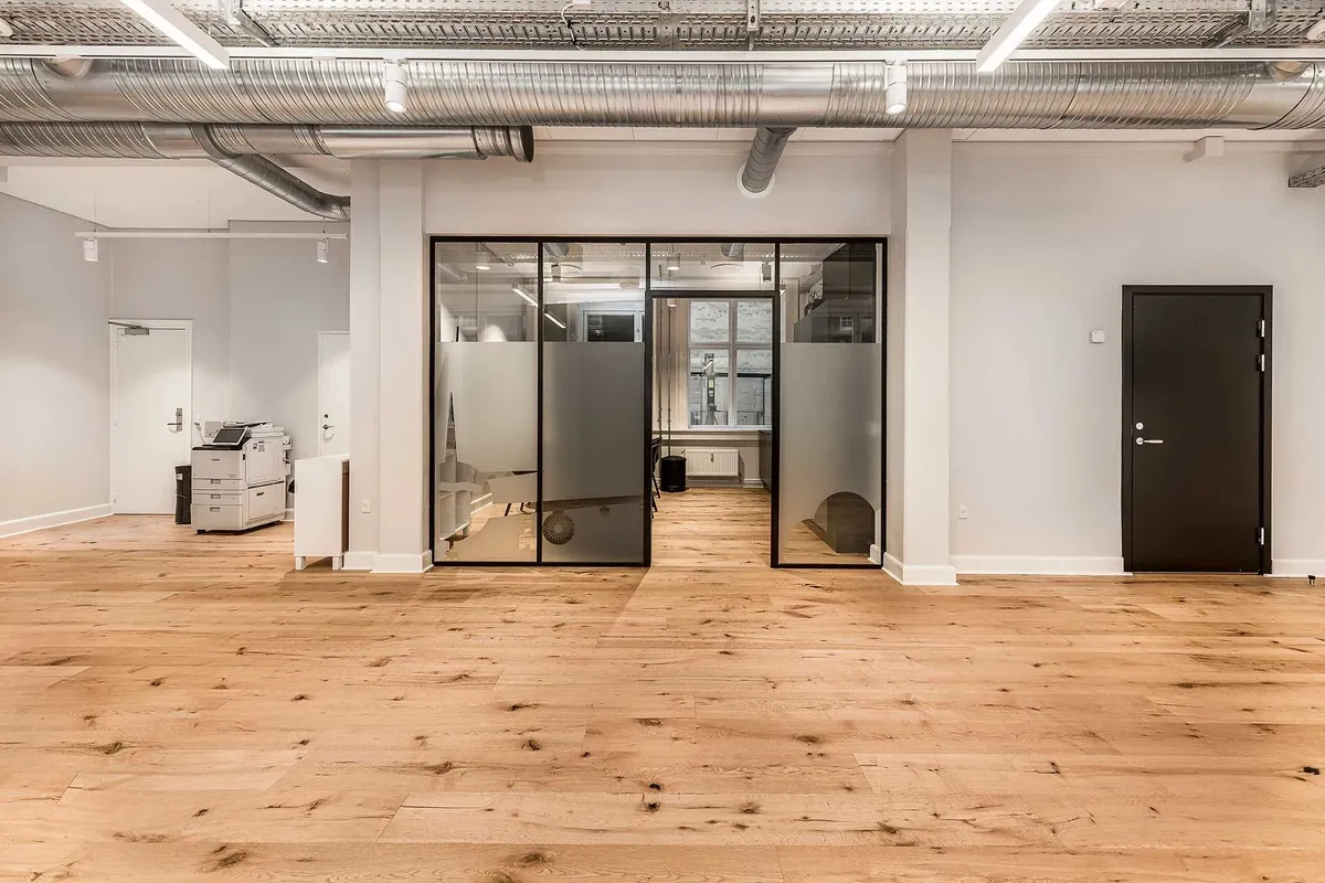 En luksuriøs kontorrum med højt til loftet, hvidt vægmaleri og lyse trægulve. Værelse med moderne glasdøre og