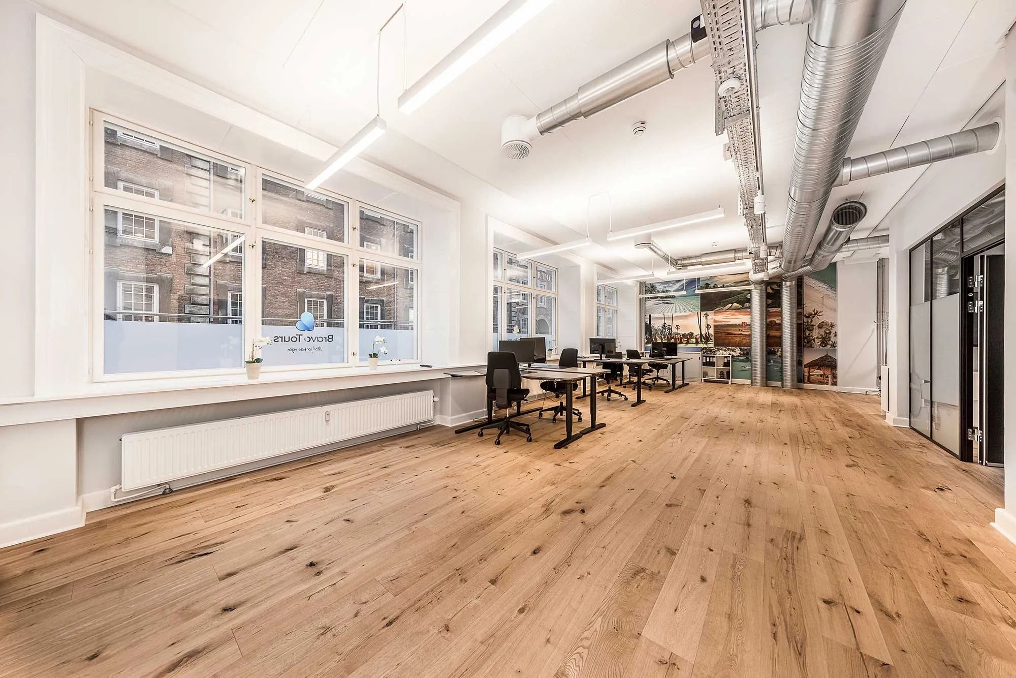 Kontor med lyse, hvide vægge og lyse trægulve samt moderne møbler, stående borde og stole