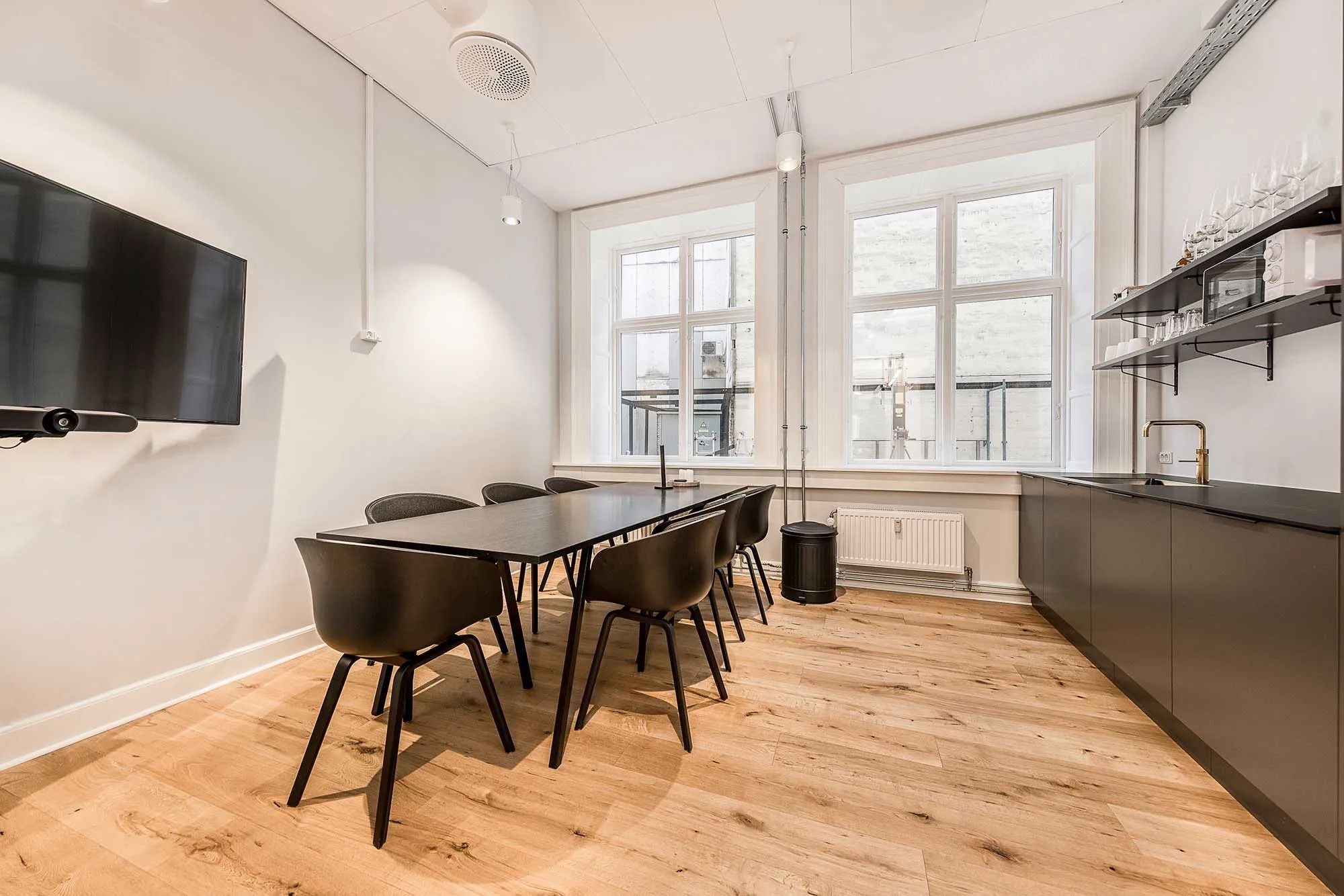 Moderne kontor med højloftede rum, massivt trægulv, minimalistisk møblering og en stor tv-skærm på væggen