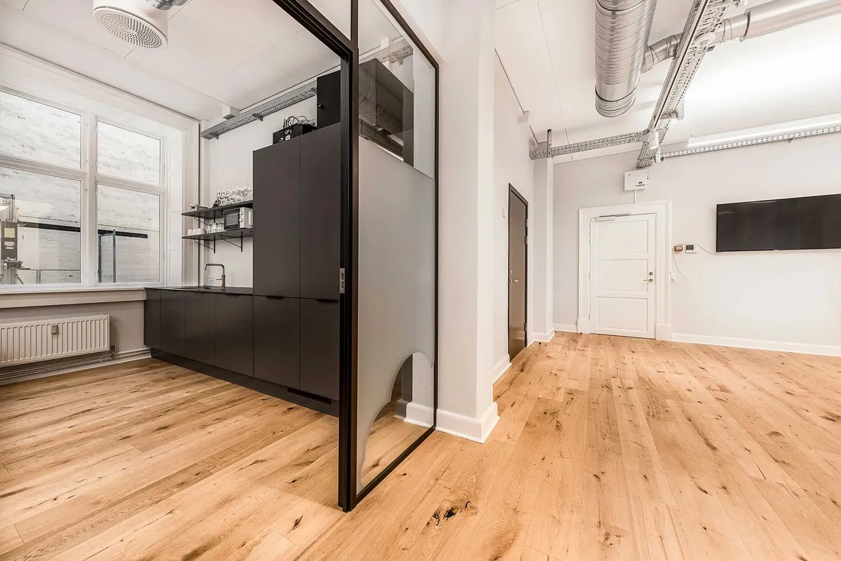 Moderne kontor med højloft og lyse trægulve, lyse vægge og minimalistisk indretning, indrammet af store vinduer med udsigt