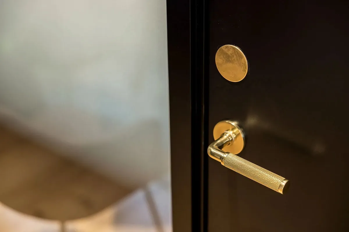 En sort dør med en guldfarvet håndtag og et guldfarvet rundt nøglehul i øverste del af døren