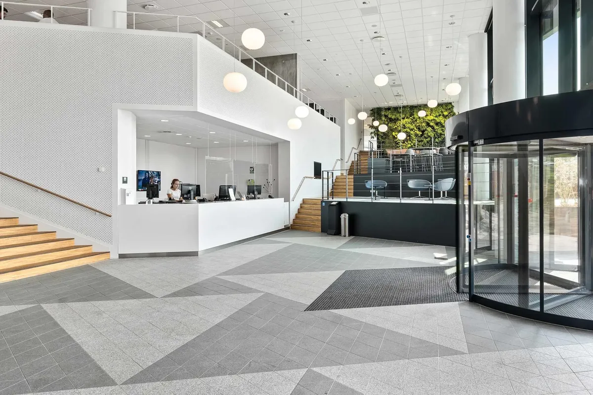 Moderne lobby med højt loft, lys og lysekroner, høj vinduesglas og indgangsdør, og stolpe med skrift og skrivebord