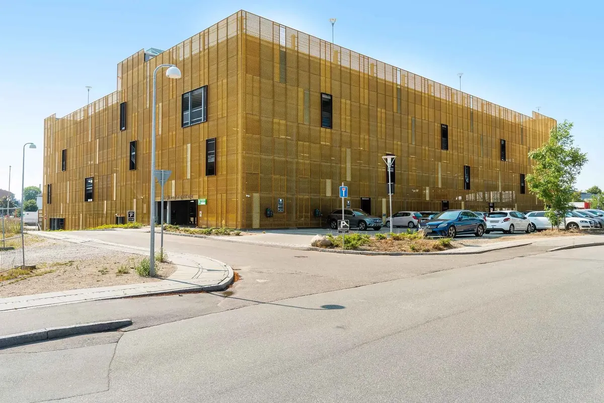 Gult kontorhus med metalgitter, parkeringsplads og parkeringsskilt samt biler og en plante