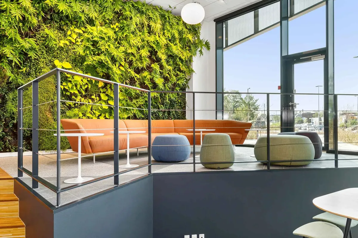 Et moderne kontor med grønne planter, orange sofa og højt til loftet med lyse vinduer og moderne møbler