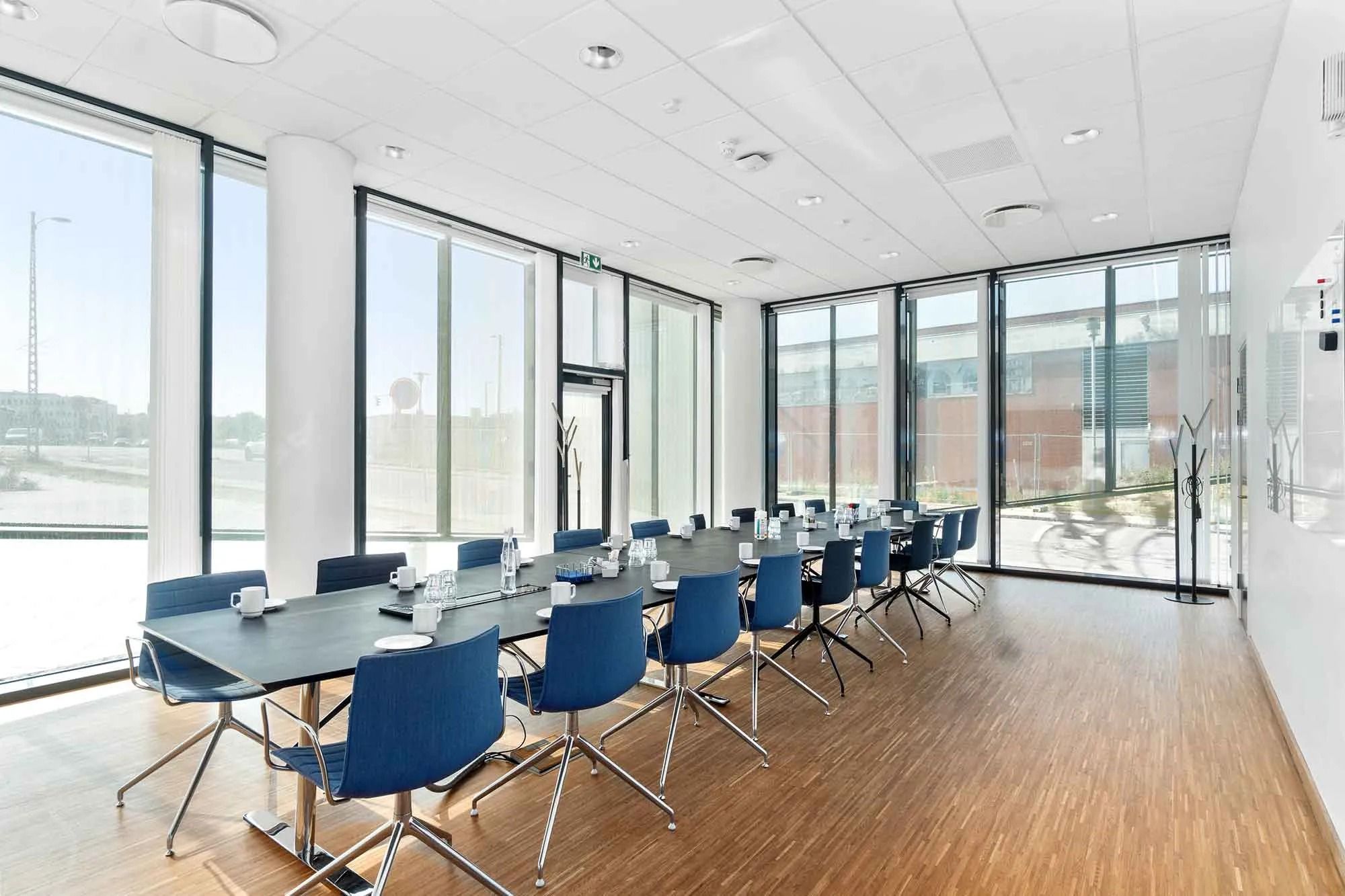 Moderne kontor med glasvinduer, møbler og tekstiler i blå og hvidt, højloftede og hvide vægge