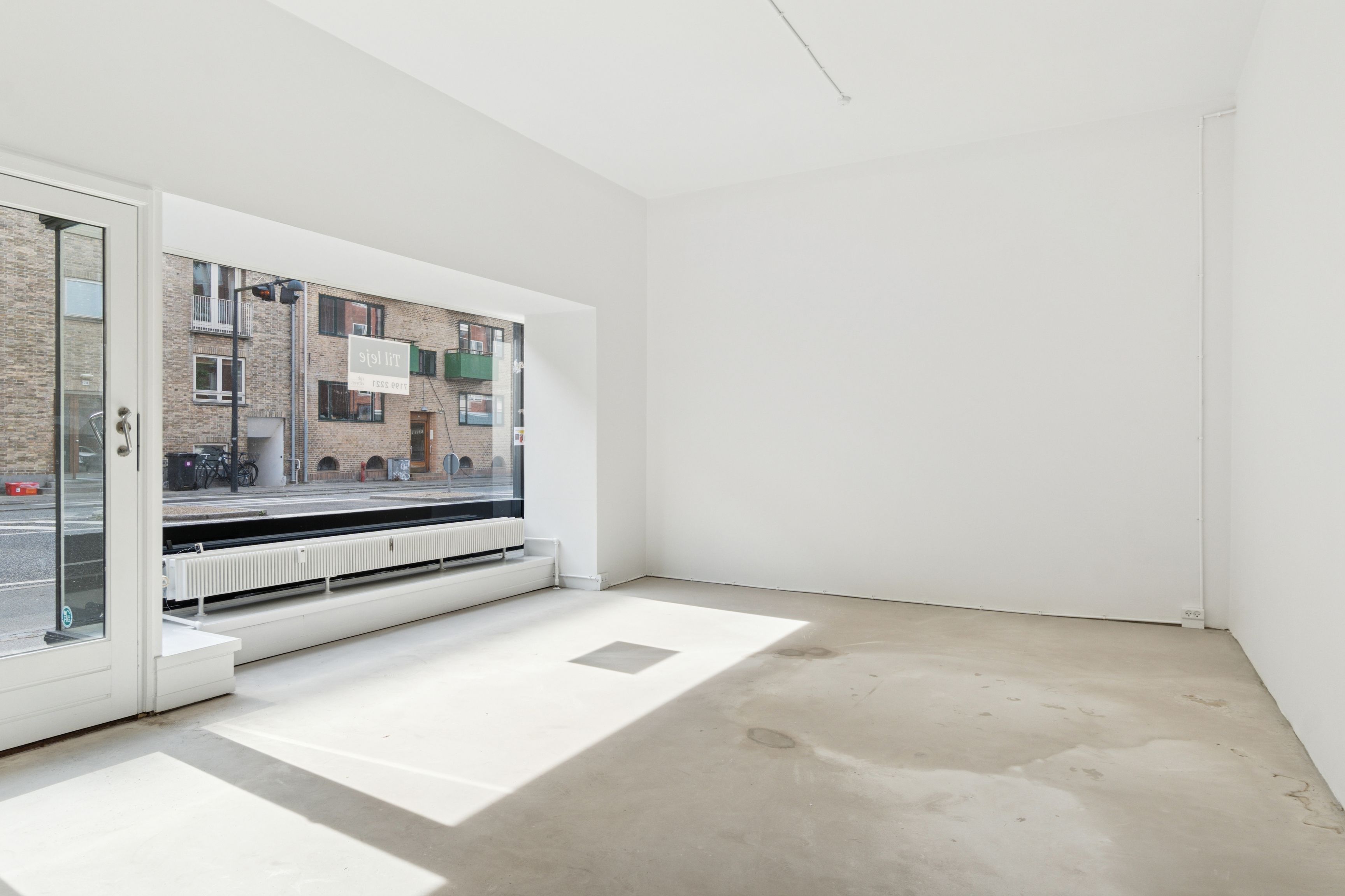 En tom butik med hvide vægge, glasdøre, en stor vinduesfront og en lagerdør i højre side.