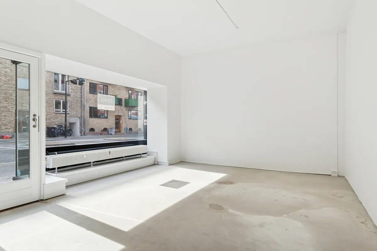 En tom butik med hvide vægge, glasdøre, en stor vinduesfront og en lagerdør i højre side.