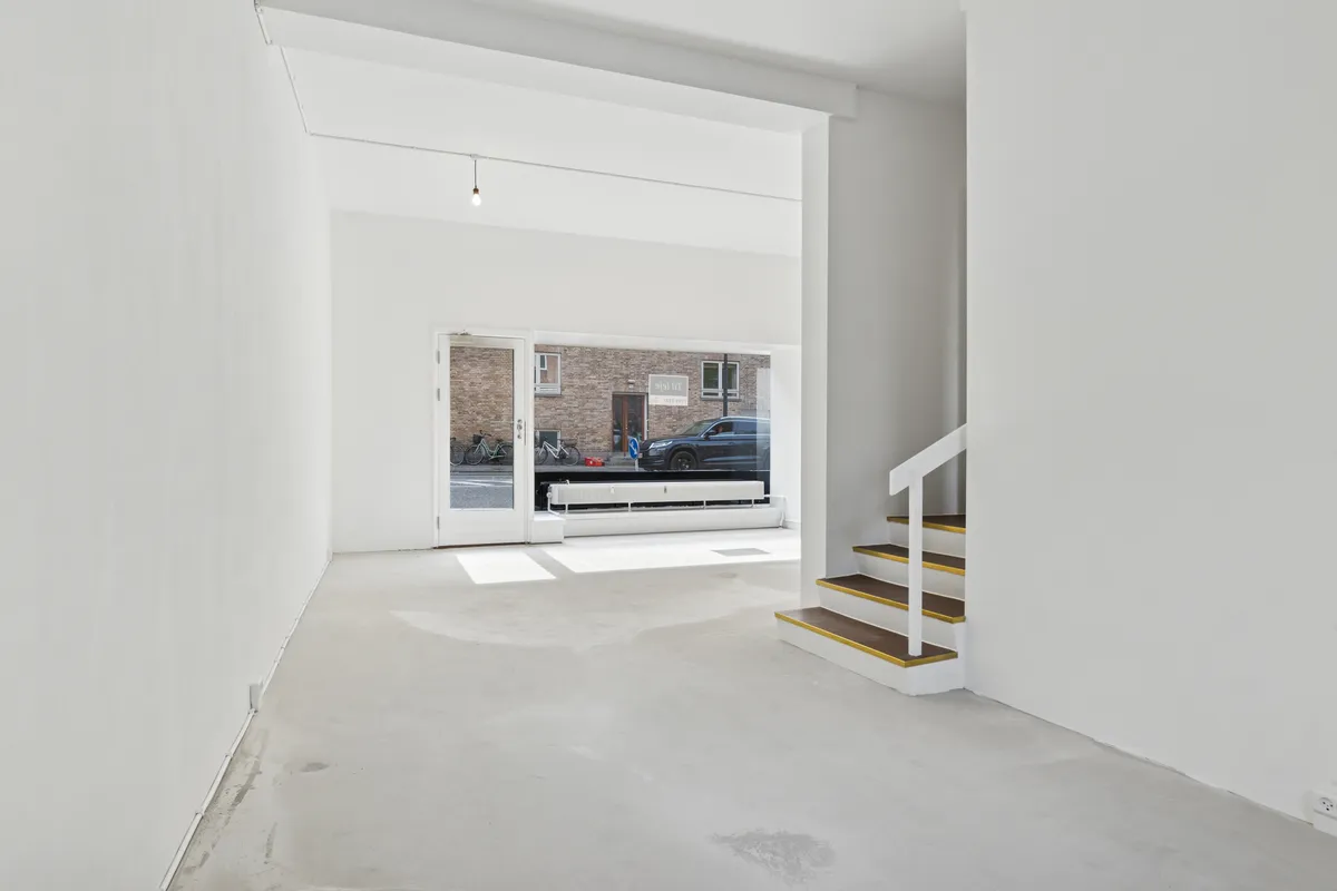 Butik med stort glasvindue mod gaden og trappe til første sal. Rummeligt og lyst salgsområde med lysegule og hvide vægge.