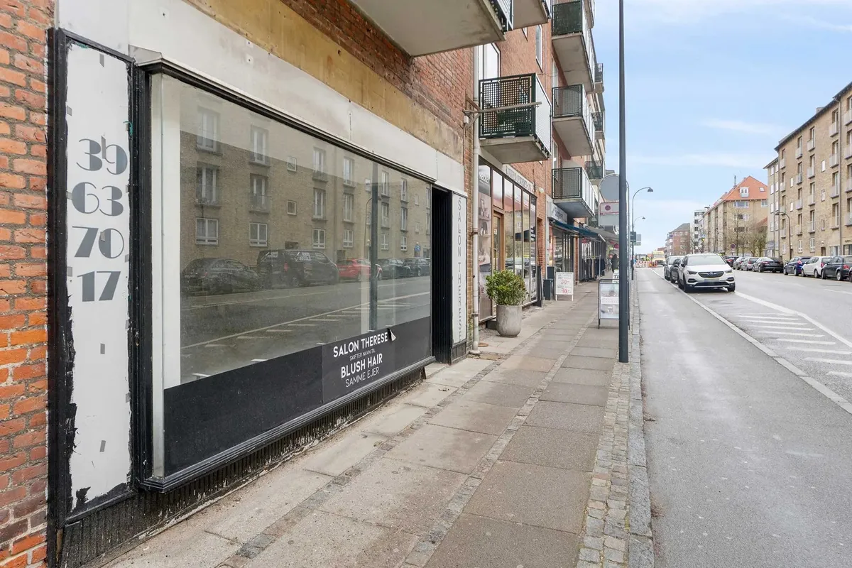 Butikslokaler i Ordrup med lager i kælderen og rummeligt salgsareal. En bil kører langs siden af gaden med parkerede biler