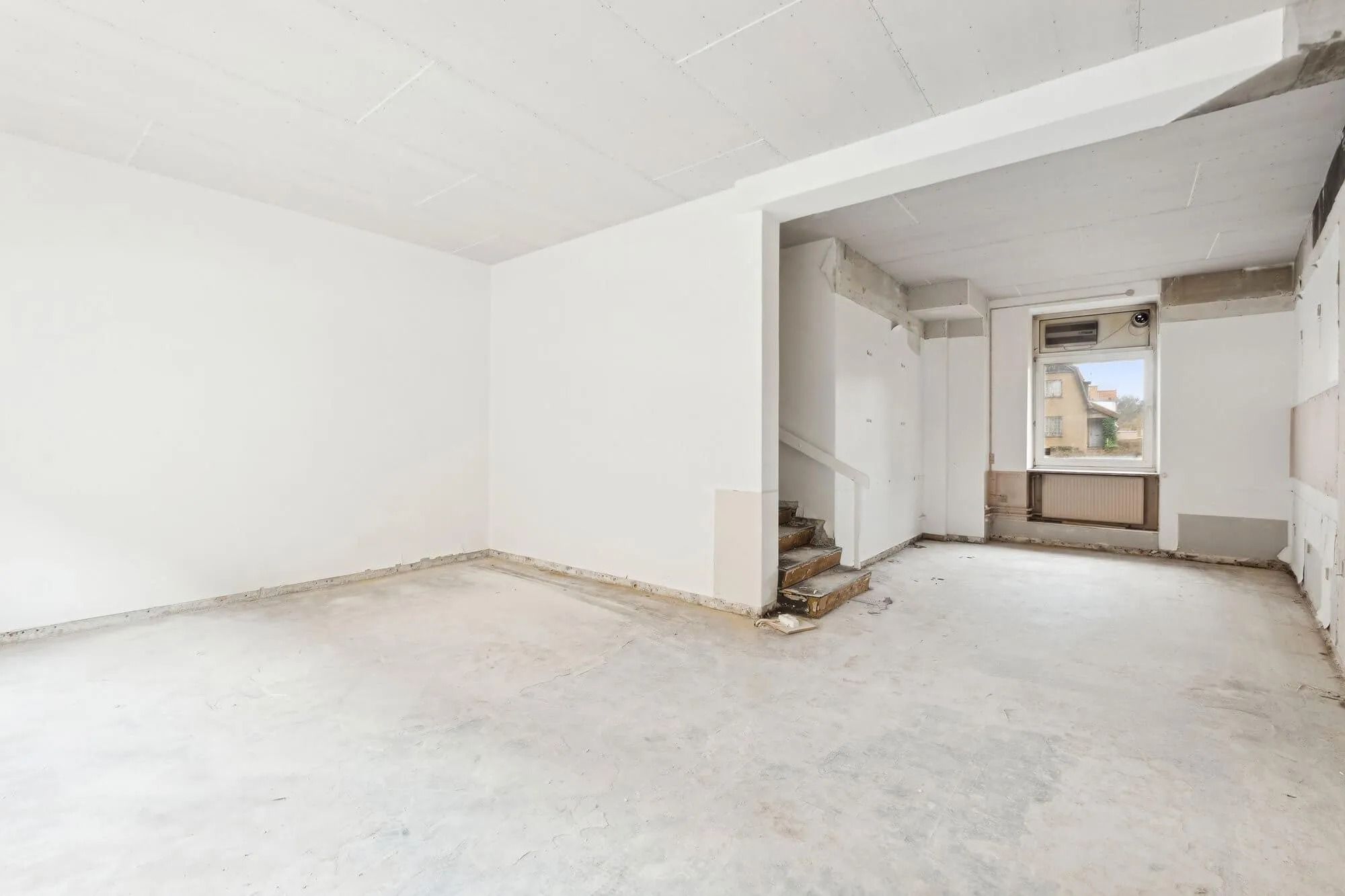 Et stort og hvidt rum med skrå hvide vægge og gulv samt et hjørne med en stig til en dør og et vindue