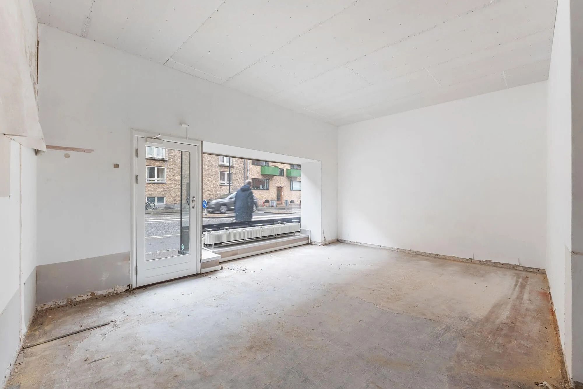 En tom butik med hvide vægge og gulve samt store vinduer mod gaden