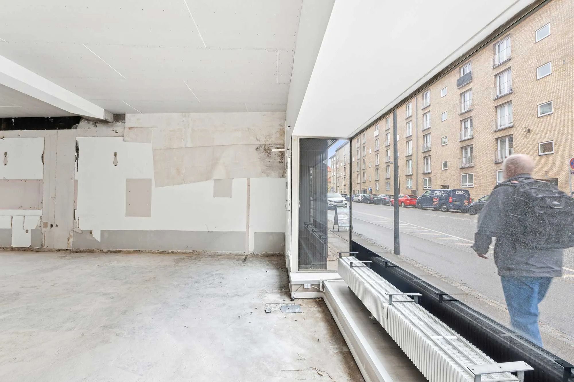 Rummeligt men ufuldendt butikslokale med trægulv og lyse vægge i hjertet af Ordrup med baggrund i et stort bygningskompleks