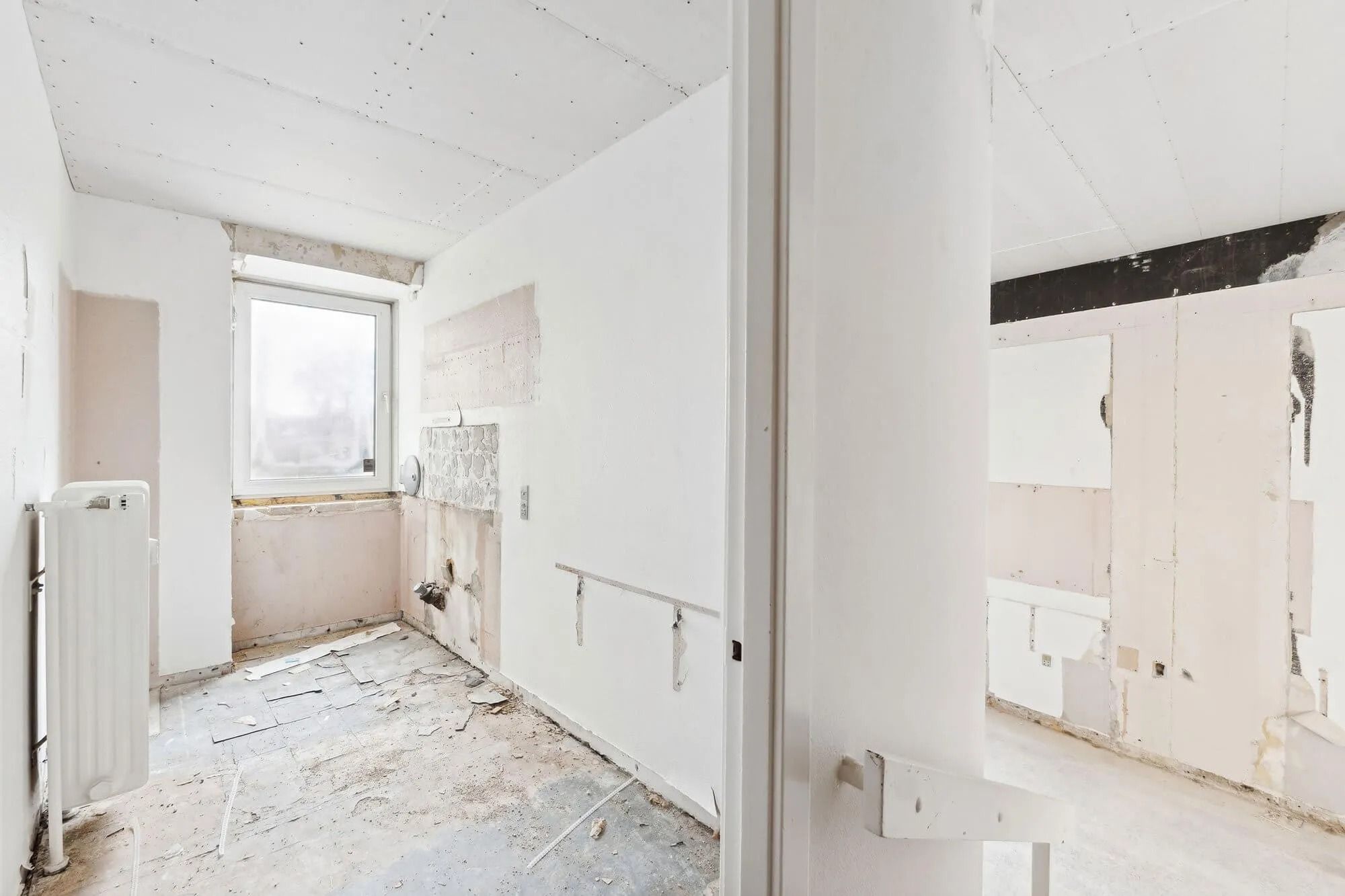 En renoveret og forladt stue med hvide vægge og loft samt en åben dør og et vindue med en hvid gardin