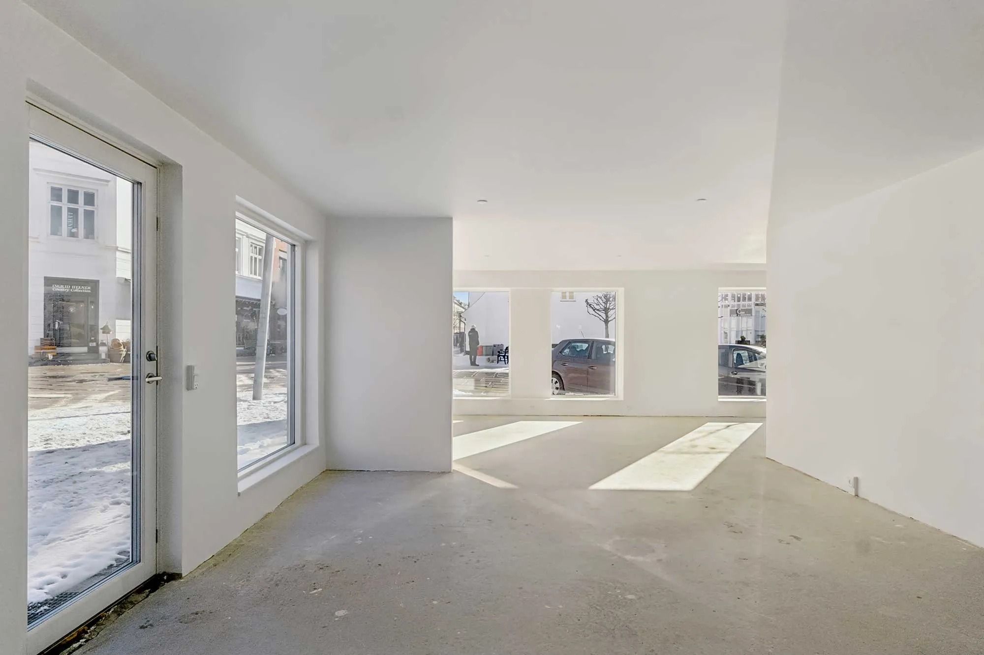 Indenfor en stor, lys og rummelig butik, med hvide vægge og store vinduer, står to biler parkeret på gade.