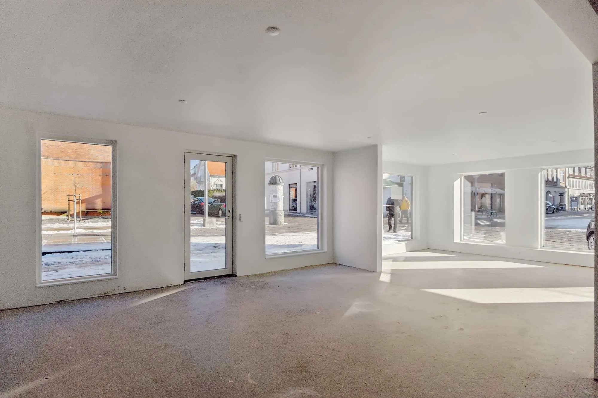 Butikslokale med store ruder og højt loft udsmykket med lysekroner og en ren hvid farvetone i indretningen